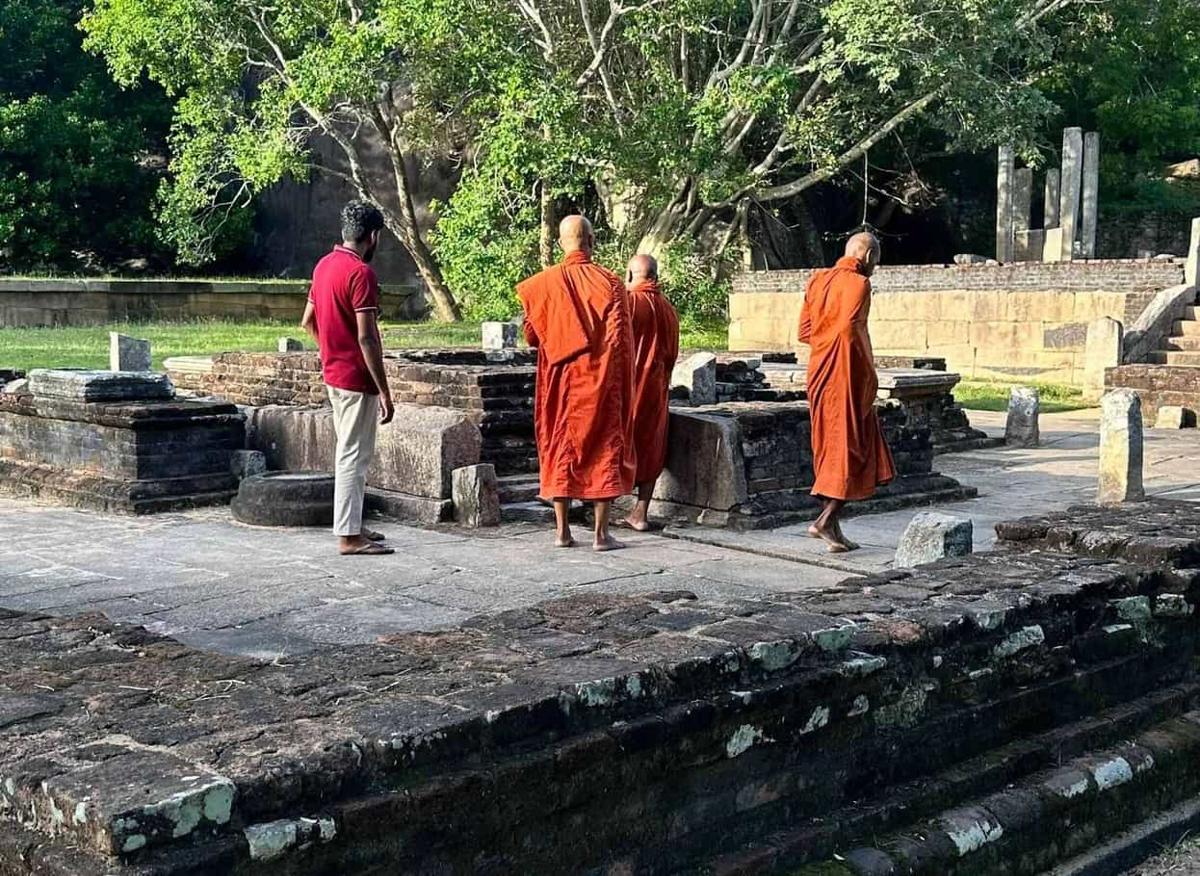 Buddhist monks in orange robes walking among ancient temple ruins near Ulpotha.