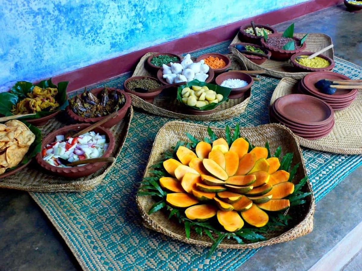 Clay bowls of curries and sambols around a spiral of cut mango and papaya, set on reed mats against a vivid blue lime-washed wall