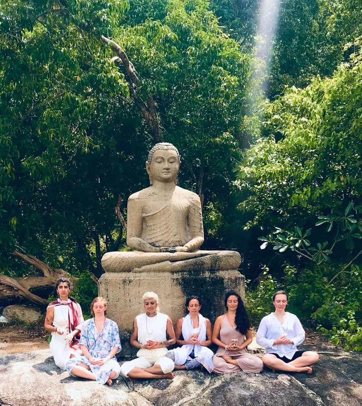 Guests in white seated on a rock before a stone Buddha in the jungle