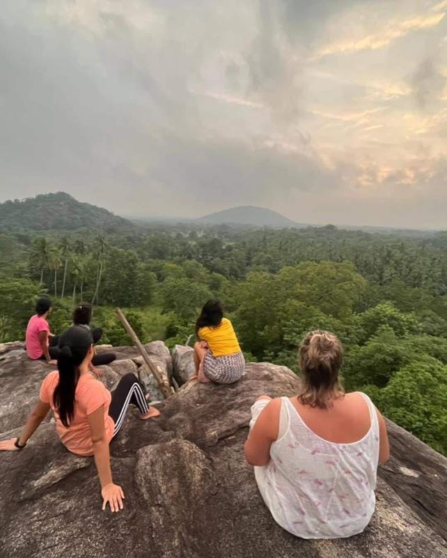 Guests sitting on a granite rock, looking out over the jungle and the hills at dusk
