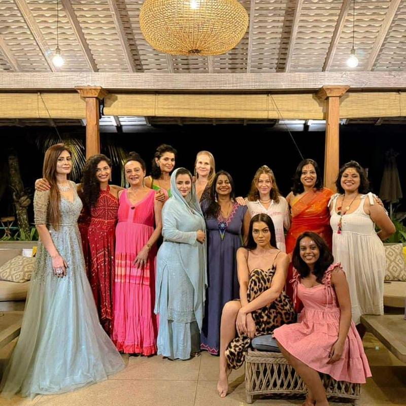 A group of women in bright dresses under a woven lamp in an open pavilion at night