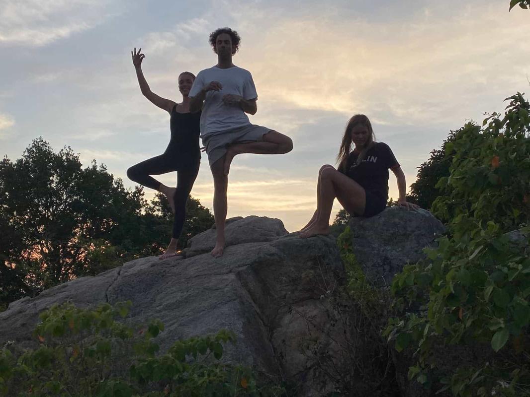 Two people in tree pose and one sitting on a boulder at dusk